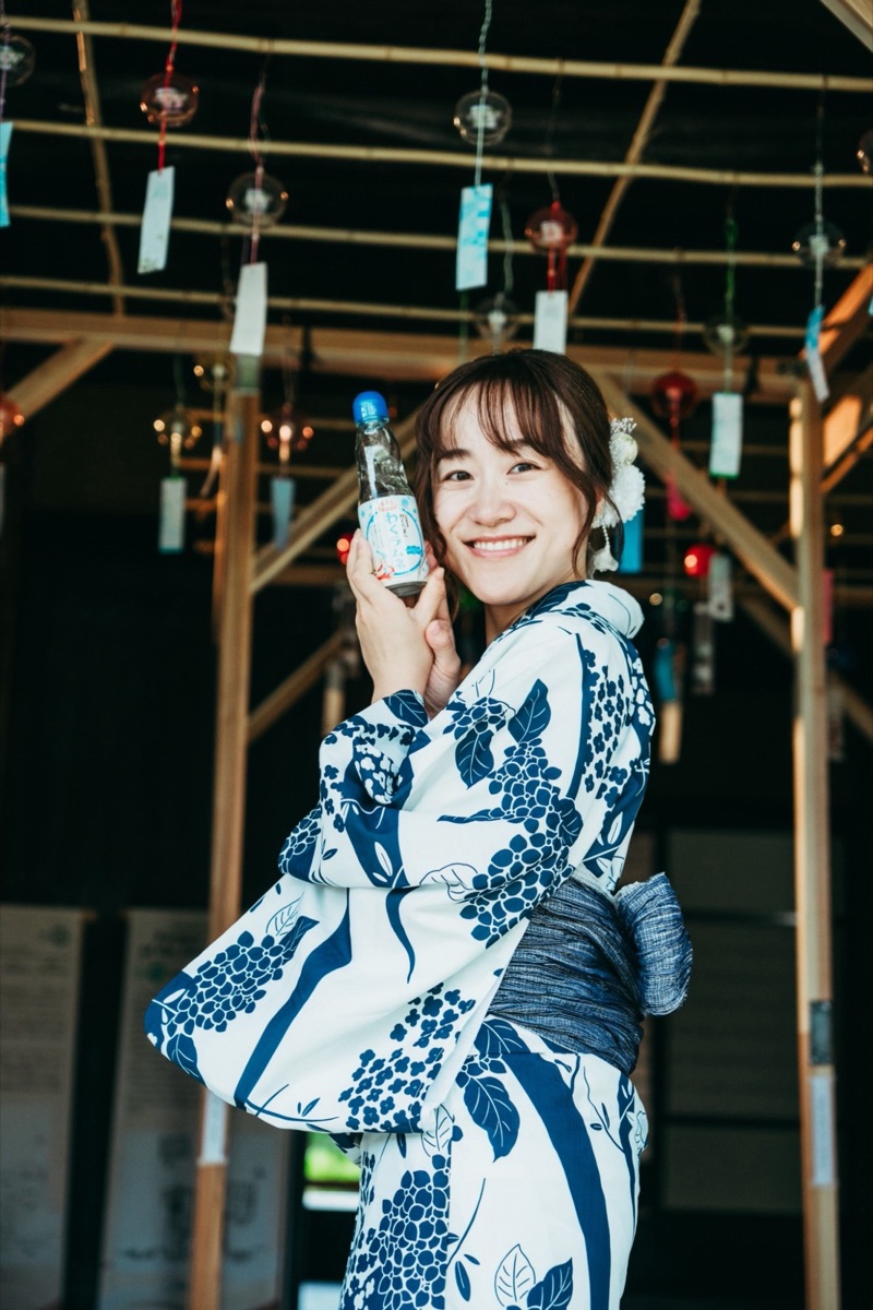 Yuri, a Kanazawa-born private guide, smiling in a blue and white summer yukata under hanging wind chimes
