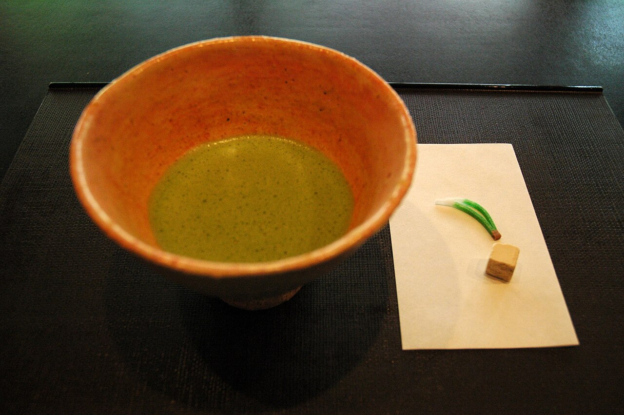 A bowl of frothy matcha next to small dry Japanese sweets on a tray