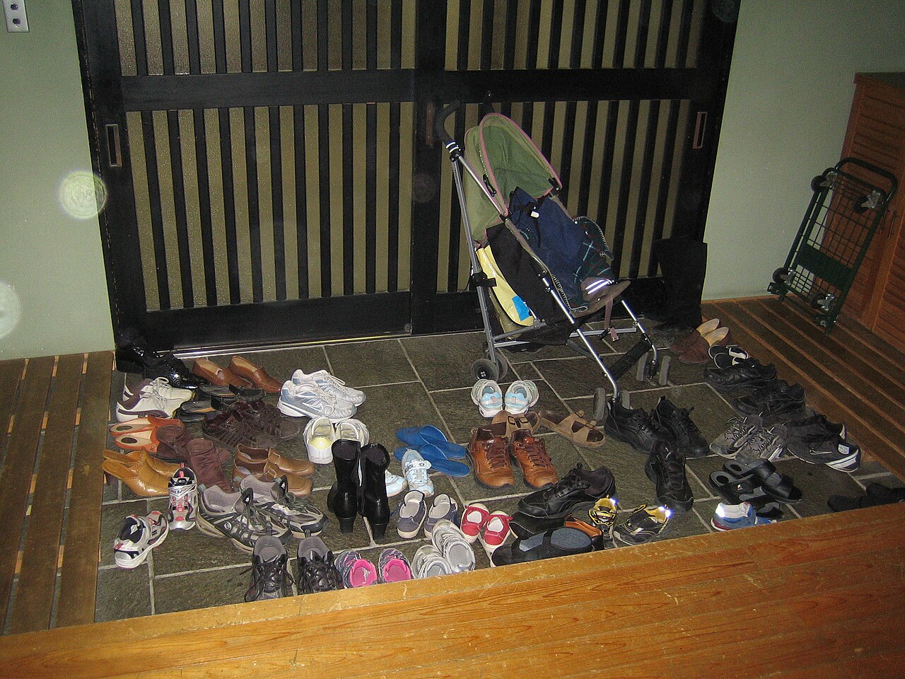 Many pairs of shoes left on the floor of a Japanese entrance before a raised wooden step