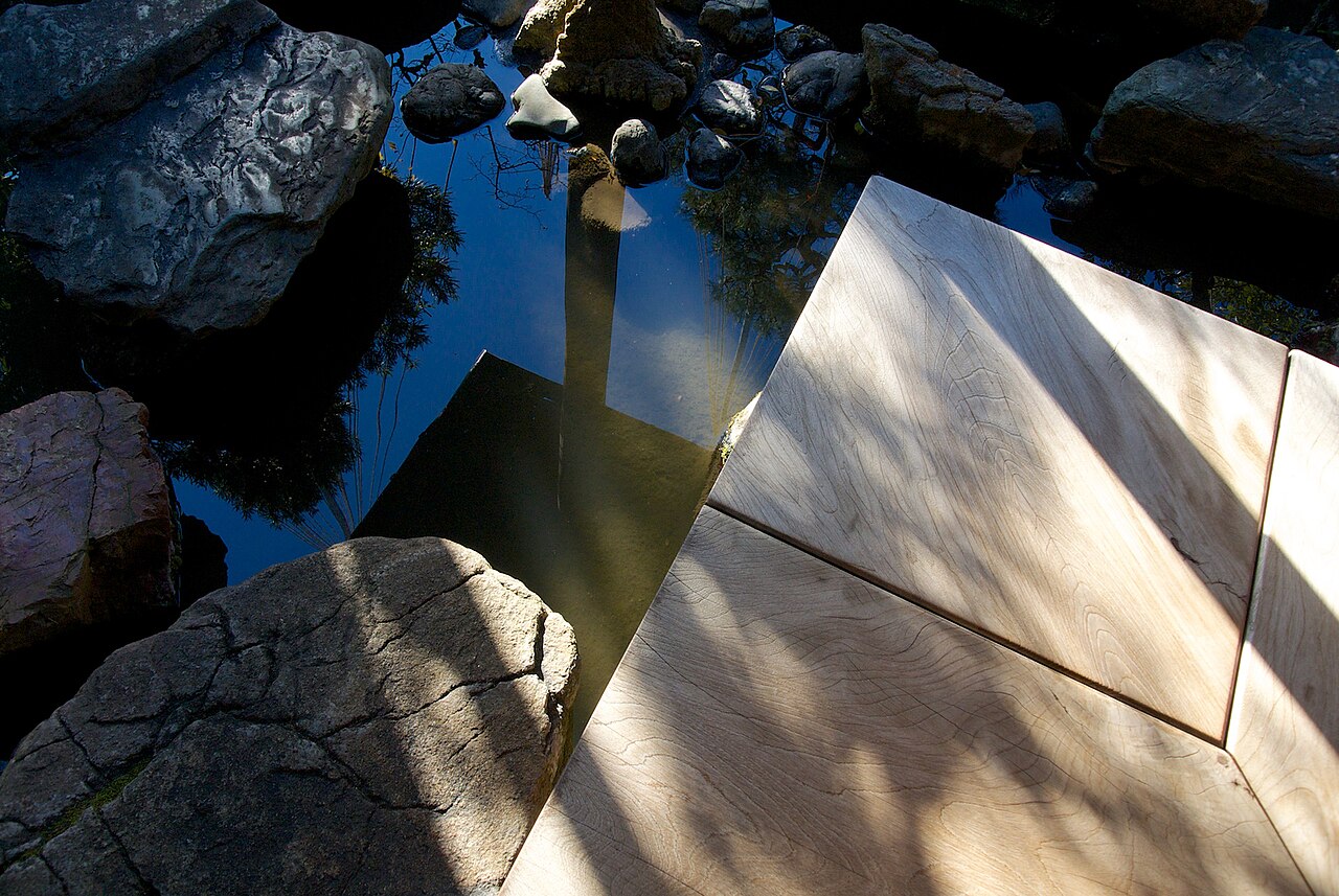 A flat stone step beside a small pond and rocks in the garden of the Nomura house